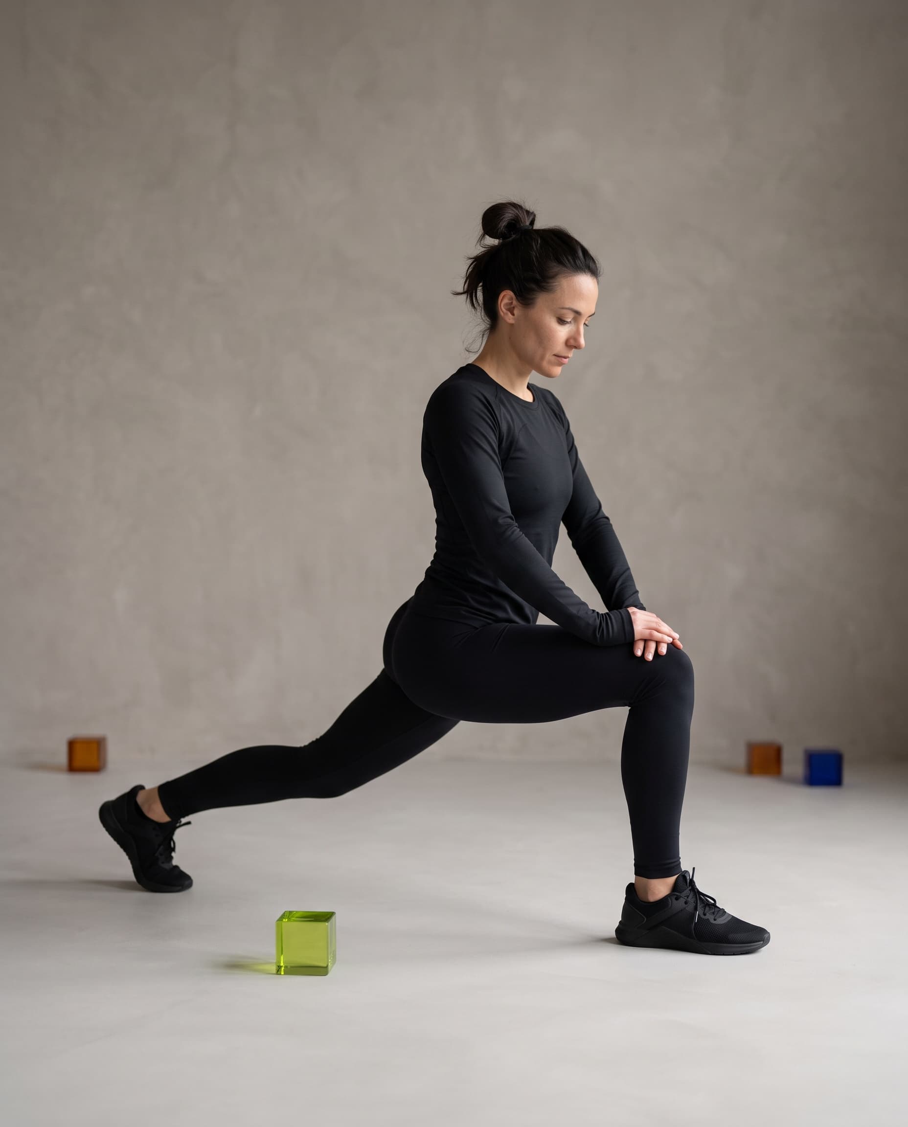 An athlete in black training wear holding a deep lunge stretch, small glass cubes on the floor